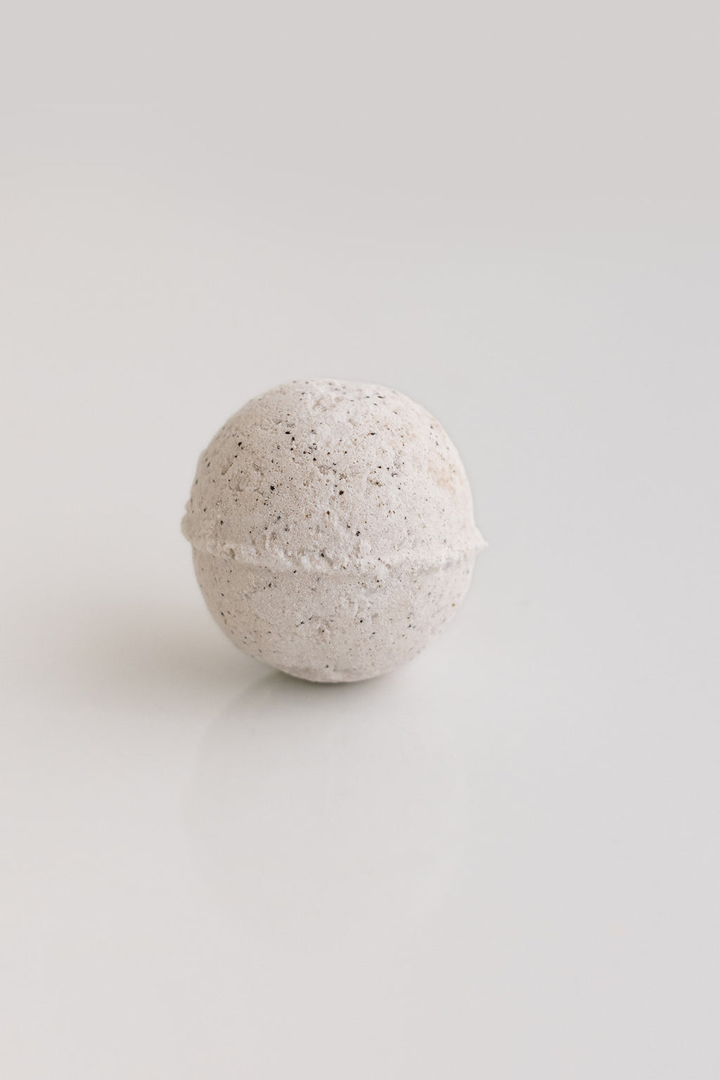 Round bath bomb with speckled texture on a light gray background