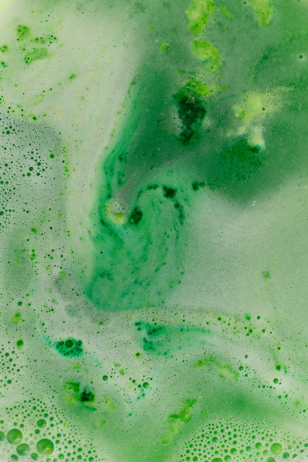 Close-up of green bath bomb溶解in water with bubbles and foam.