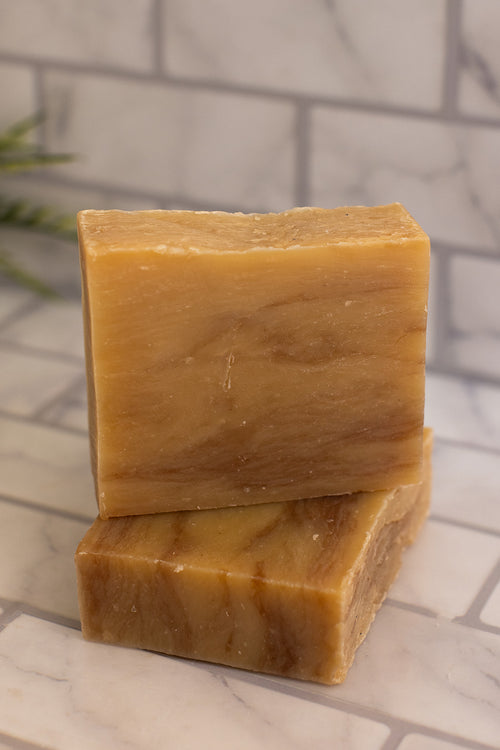 Two bars of brown soap stacked on a marble surface with a tiled wall background