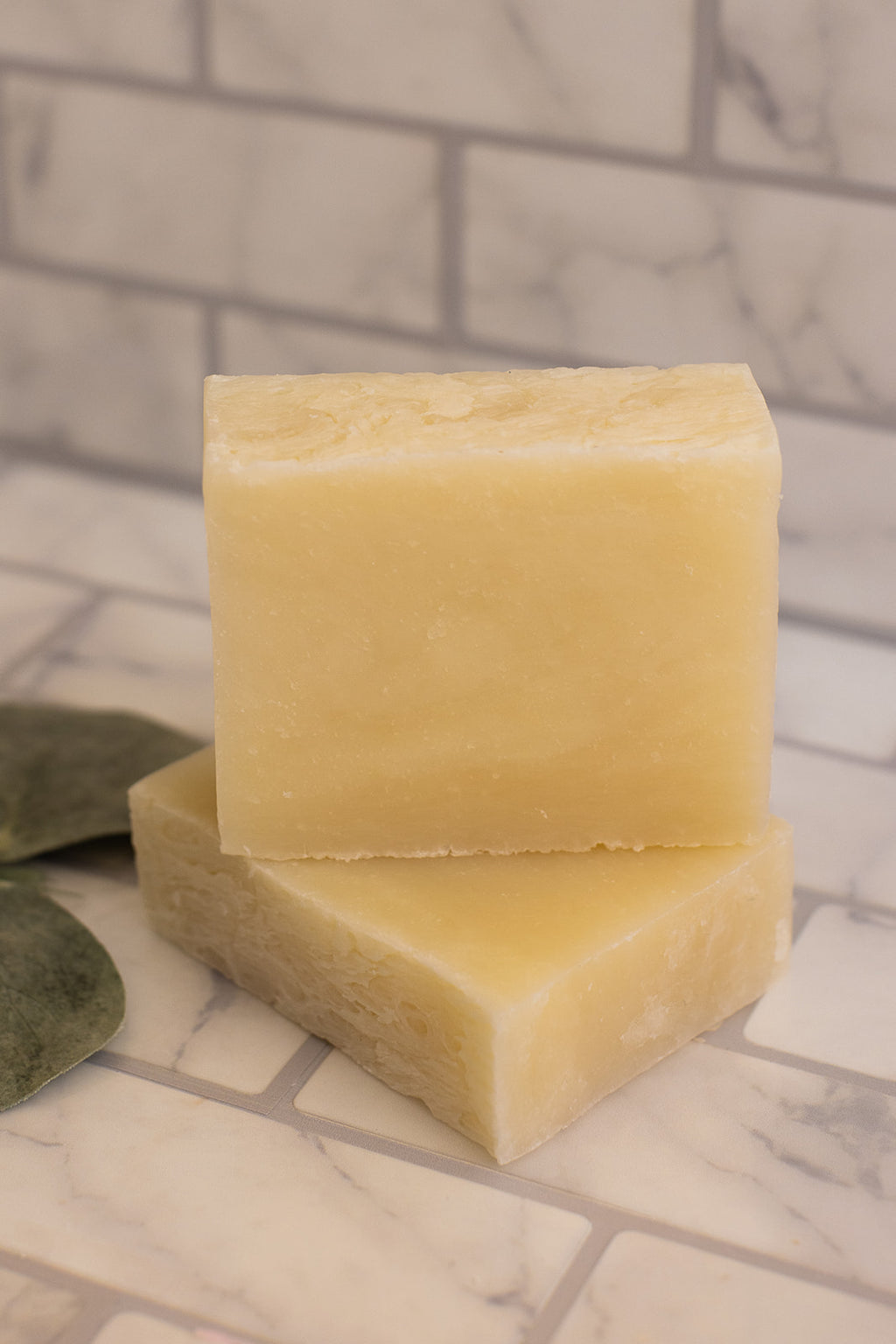 Two yellow soap bars stacked on a marble surface with a tiled wall background