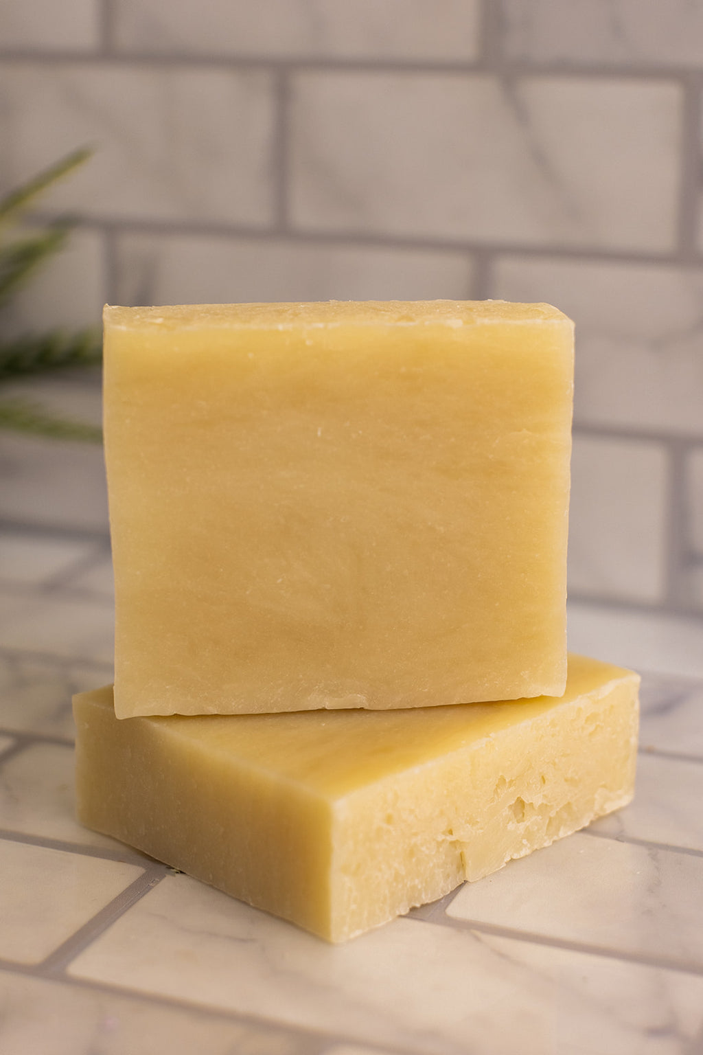 Two yellow soap bars stacked on a tiled surface with a blurred bathroom background.
