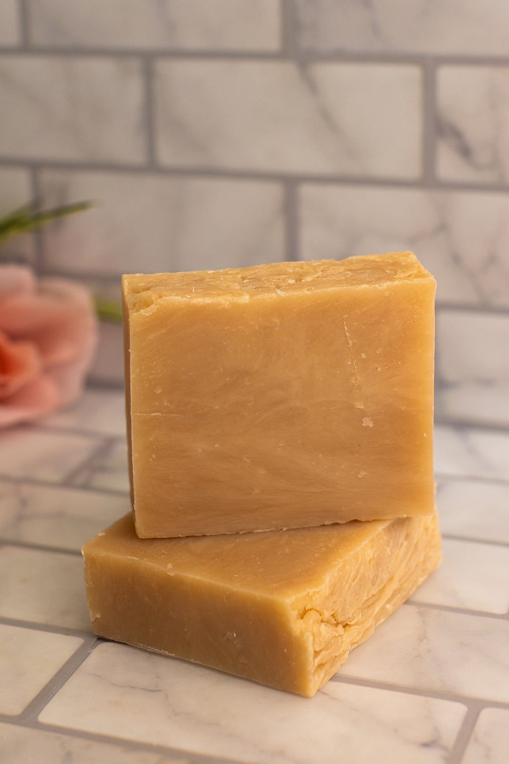 Two bars of yellow soap stacked on a tiled surface with a blurred background